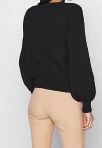 Schwarzer gerippter Strickpullover mit lockerer Passform und Ballonärmeln, kombiniert mit hellbeigen, eng anliegenden Hosen. Strukturiertes Material mit umgeschlagenen Säumen.