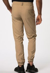Los joggers de cintura elástica en color beige presentan puños fruncidos, un bolsillo trasero y una textura suave, combinados con zapatillas deportivas negras.