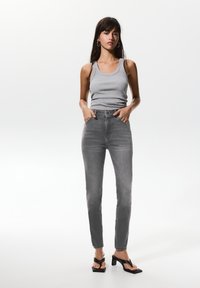 Jeans gris à taille haute, jambes droites et poches avant, associés à un débardeur gris ajusté et des sandales à talons noires.