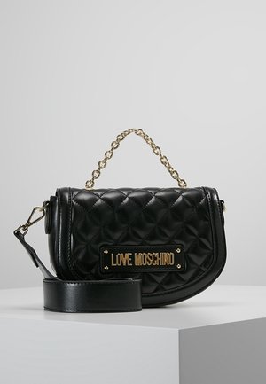 Czarna pikowana skórzana torebka na złotym łańcuszkowym uchwycie z metalową plakietką z napisem "LOVE MOSCHINO" na przodzie, spoczywająca na białej powierzchni.