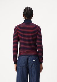 Pull col roulé à rayures bleu marine et rouge à manches longues avec poignets et col côtelés, présentant une coupe ajustée et une texture douce.