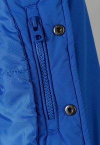Tessuto in nylon blu con chiusura a zip e bottone a pressione metallico. Superficie testurizzata con dettagli cuciti. Leggero e liscio.
