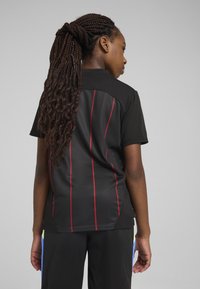 Zwart sportshirt met korte mouwen, voorzien van rode verticale strepen op de rug en een platte kraag, gemaakt van gestructureerde stof.
