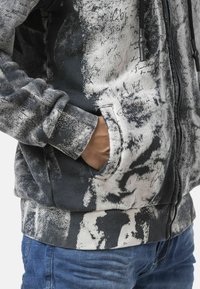 Grijze en zwarte hoodie met abstracte print. Voorzien van een voorkantzak en geribbelde manchetten. Het materiaal heeft een gestructureerde uitstraling.