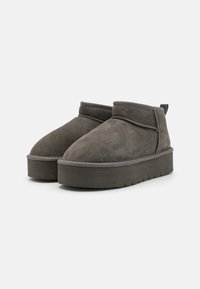 Stivali ankle in suede grigi con punta rotonda, suola spessa e piattaforma, e dettagli di cucitura sottili. Texture morbida e design minimalista.