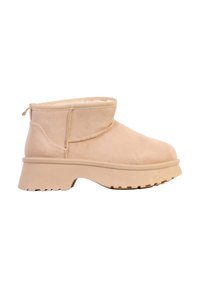 Bottines en daim beige avec un design à enfiler, un talon bloc bas et une semelle extérieure en caoutchouc texturé pour une meilleure adhérence. Doublure intérieure douce visible.