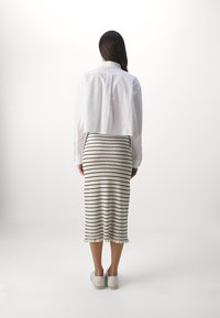 Camisa blanca corta sobre una falda crema de longitud hasta la rodilla con rayas negras y un dobladillo con volantes, combinada con unos zapatos blancos sin cordones.