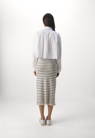 White cropped shirt over a knee-length cream skirt with black stripes and ruffled hem, paired with white slip-on shoes.