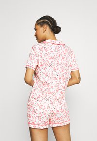 Floral short-sleeve pajama set featuring a pink and white pattern, soft fabric, contrasting piping, and a relaxed fit for comfort.