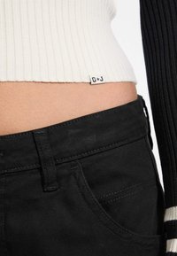 Črne jeans hlače z visokim pasom, z vidnim žepom in kontrastnim rebrastim materialom v beli in črni barvi na vrhu, označene z G+J.