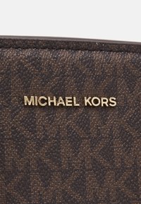 Tessuto marrone a motivi con superficie texturizzata. Presenta un logo dorato "Michael Kors". I bordi sono cuciti in modo uniforme.