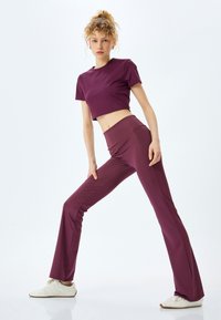 Paarse cropped sporttop gecombineerd met bijpassende paarse flared broek. De stof lijkt soepel en rekbaar. Witte sportschoenen maken de outfit compleet.