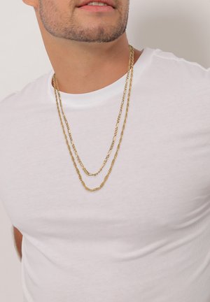Guld metal kæden Halskæder i forskellige længder lagdelt over en hvid t-shirt, med snoede og flade led.