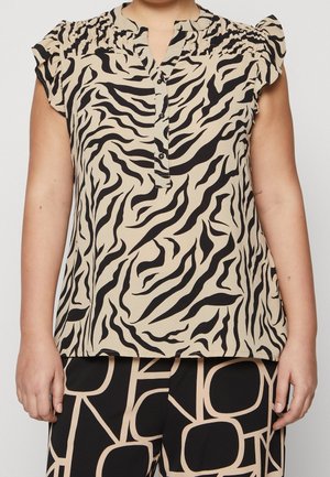 Beżowa i czarna bluzka w zebra print z krótkimi rękawami i falbankami na ramionach, zestawiona z czarnymi spodniami ozdobionymi dużymi beżowymi abstrakcyjnymi literami.