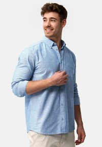 Lyseblå button-up skjorte lavet af tekstureret stof. Har en brystlomme, knapmanchetter og en afslappet pasform. Glat tekstur og klassisk design.