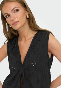 Zwarte geborduurde blouse met een diepe V-hals, mouwloos ontwerp, bloemen uitsnijdingen en een striksluiting aan de voorkant. Gestructureerde stof.