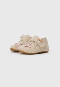 Pantoufles en feutre de couleur beige clair avec une texture douce, dotées d'une sangle en Velcro et d'appliqués en forme de fleur rose à l'avant. Semelles en caoutchouc marron.