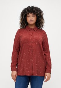 Chemise boutonnée bordeaux à manches longues, avec col et motif de pois blancs. Comprend deux poches poitrine et une texture lisse.