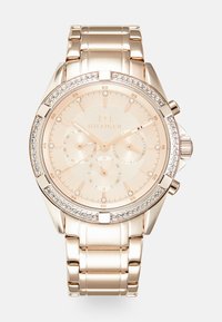 Montre en acier inoxydable rose doré avec un boîtier rond, une lunette décorée de cristaux, trois sous-cadrans, et un cadran beige avec des marqueurs d'heure minimalistes.