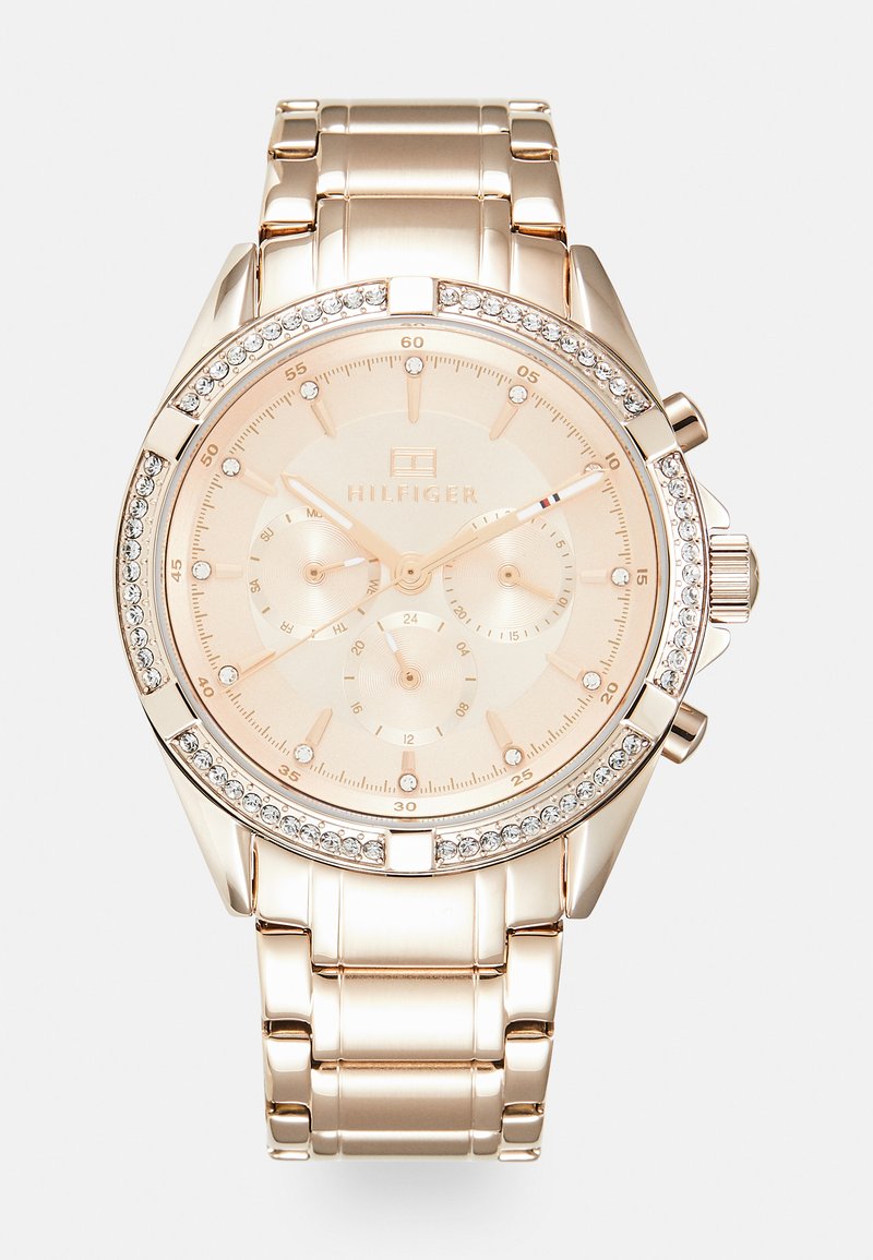 Montre en acier inoxydable rose doré avec un boîtier rond, une lunette décorée de cristaux, trois sous-cadrans, et un cadran beige avec des marqueurs d'heure minimalistes.