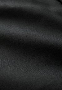Tissu noir avec une surface texturée, présentant un motif légèrement ondulé. Le tissage est serré, créant une apparence de matériau lisse mais durable.