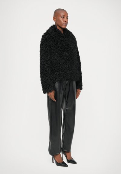 Μαύρο φ fuzzy εξωτερικό ρούχο με φαρδύ γιακά, σε συνδυασμό με κομψά μαύρα δερμάτινα παντελόνια και μυτερές μαύρες γόβες. Λείος υφή και δομημένος σχεδιασμός.