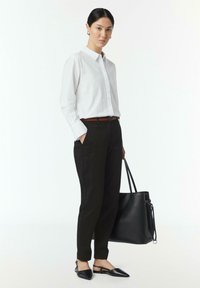 Witte lange mouwen knopshirt, zwarte slim-fit broek, bruine riem en zwarte tote bag; zwarte flats met punt en enkelriemen.