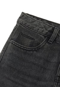 Un bolsillo de jeans de mezclilla negra con costuras visibles y un lazo para cinturón sobre un fondo blanco.