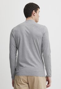 Camisa gris de manga larga con cuello redondo, hecha de una suave mezcla de algodón. Presenta un ajuste holgado y sutiles aberturas en los laterales del dobladillo.