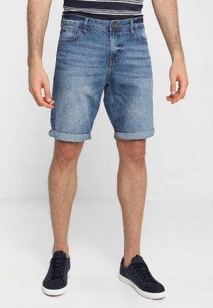 Lichtblauwe denim shorts met opgerolde pijpen, vijf zakken en een knoopsluiting aan de voorkant, gecombineerd met donkerblauwe sneakers.