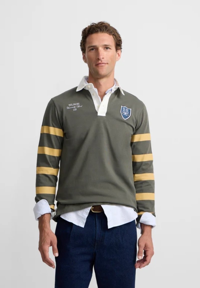 Camiseta de rugby de manga larga verde con cuello blanco, rayas amarillas en las mangas y logo de escudo bordado en el pecho. Corte clásico y tejido texturizado.