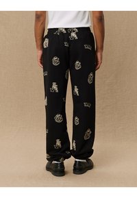 Zwarte sweatpants met een relaxte pasvorm, voorzien van bruisende graphics van beren en "Yale"-logo's in een tan kleur. Gemaakt van zachte stof, met elastische boorden bij de enkels.