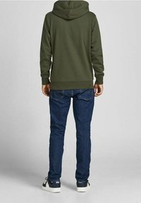 Felpa verde oliva con cappuccio, tasche laterali doppie e polsini a costine, abbinata a jeans blu e sneaker bianco e nere.