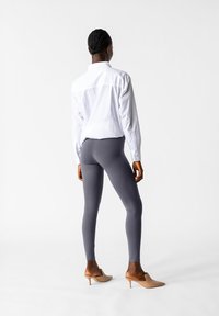 Leggings grigi abbinati a una camicia bianca con bottoni e scarpe con tacco beige. Le leggings presentano una superficie liscia e un design aderente.
