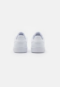 Des baskets blanches avec une tige en cuir lisse, un talon arrondi et une semelle en caoutchouc texturé. "Stan Smith" embossé à l'arrière.