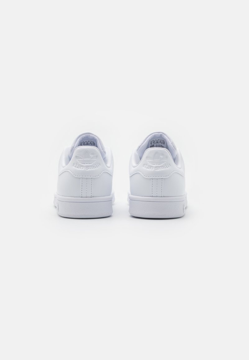 Des baskets blanches avec une tige en cuir lisse, un talon arrondi et une semelle en caoutchouc texturé. "Stan Smith" embossé à l'arrière.