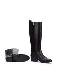 Botas negras hasta la rodilla, fabricadas en cuero suave y ante, con cremallera lateral y tacón bajo; suela de goma texturizada con patrones de agarre.