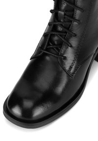 Czarne skórzane botki za kostkę z okrągłym noskiem, sznurowanym wzorem i gładką fakturą. Posiadają solidną czarną podeszwę oraz subtelne detale przeszycia.