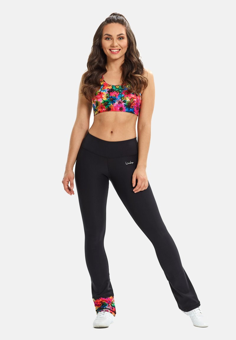 Sujetador deportivo multicolor con estampado floral combinado con leggings negros de tiro alto con ribete floral en el dobladillo, diseñados para ropa deportiva.