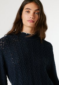 Tumesinine kudum-sviiter, millel on tekstuuriga lehtede muster, ribaga ümmargune kaelus ja laiad pikad varrukad.