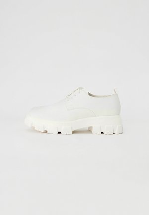 Weiße Schnürschuhe mit glatter Textur, ausgestattet mit einer stabilen, geriffelten Sohle und minimalistischem Design. Dezente Steppnähte im Obermaterial.