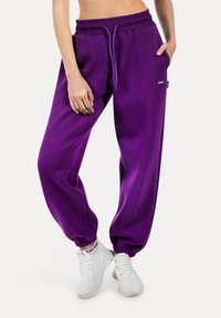 Lila Sweatpants mit lockerer Passform, elastischem Bund und Bündchen. Sie verfügen über seitliche Taschen und ein kleines Markenlogo auf der Vorderseite.