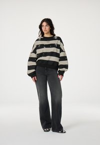 Zwarte en beige gestreepte sweatshirt met een oversized silhouet, voorzien van metallic versieringen en geribbelde manchetten, gecombineerd met donkere flared jeans.