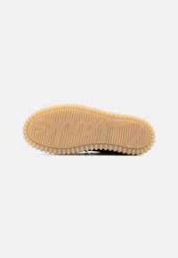 Τακούνι παπουτσιού από ανοιχτό καφέ καουτσούκ με βαθιές αυλακώσεις και στρογγυλές λαβές κατά μήκος της άκρης, με στρογγυλεμένο όνομα εμπορικού σήματος χαραγμένο στο κάτω μέρος.