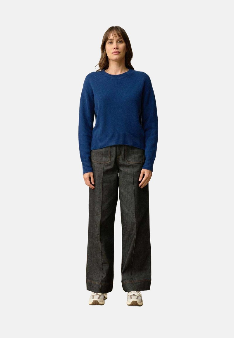 Niebieski sweter dziany z okrągłym dekoltem, w połączeniu z jasnoniebieskimi spodniami dżinsowymi o wysokim stanie i białymi trampkami. Prosty i casualowy design.