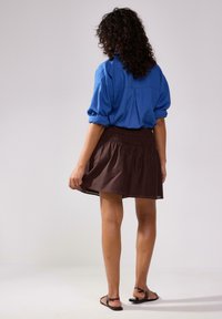 Blå skjorte med knaplukning og optrillede ærmer samt rygslids, parret med en brun A-formet nederdel med elastisk talje og flade sandaler.