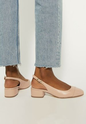 Pale pink slingback shoes with a low block heel, glossy finish, rounded toe, and adjustable buckle detail. Worn with frayed light blue jeans.