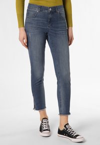 Smala jeans i blekblått med fransade kanter. Stärkt med en grön topp och svarta Converse-sneakers, vilket visar en avslappnad look.