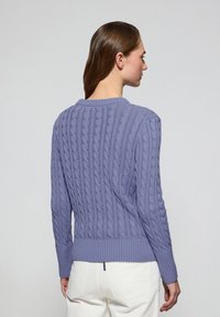 Lila kabelstickad tröja med ribbat avslut och muddar, med en texturerad vävstruktur. Enkel rund halsringning och åtsittande siluett.