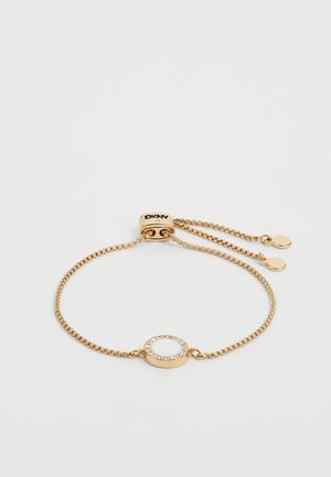 Gullfarget armbånd med en tynn kjede, som har et sirkelformet midtpunkt prydet med klare krystaller og en merket lås.